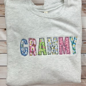 Może przedstawiać: Szara bluza z haftem "GRAMMY" wykonanym z kolorowej tkaniny kwiatowej.