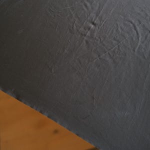 Puede incluir: Primer plano de una tela gris oscuro con arrugas y pliegues visibles. La tela parece estar drapeada, con una porci&oacute;n de una superficie marr&oacute;n claro visible en la esquina. La textura de la tela es prominente.