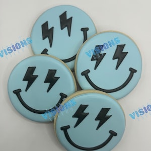 May include: Four round sugar cookies with light blue icing. Each cookie features a black smiley face with lightning bolt eyes. The cookies are arranged in a slightly overlapping pattern, showcasing their decorative design.