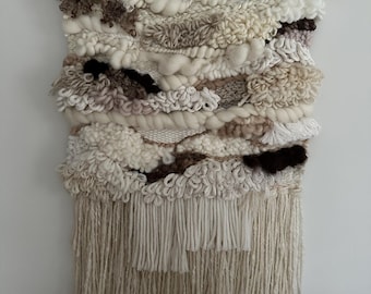 May include: A beige and brown woven wall hanging with a fringe border. The hanging is made with different textures of yarn and is attached to a wooden dowel.