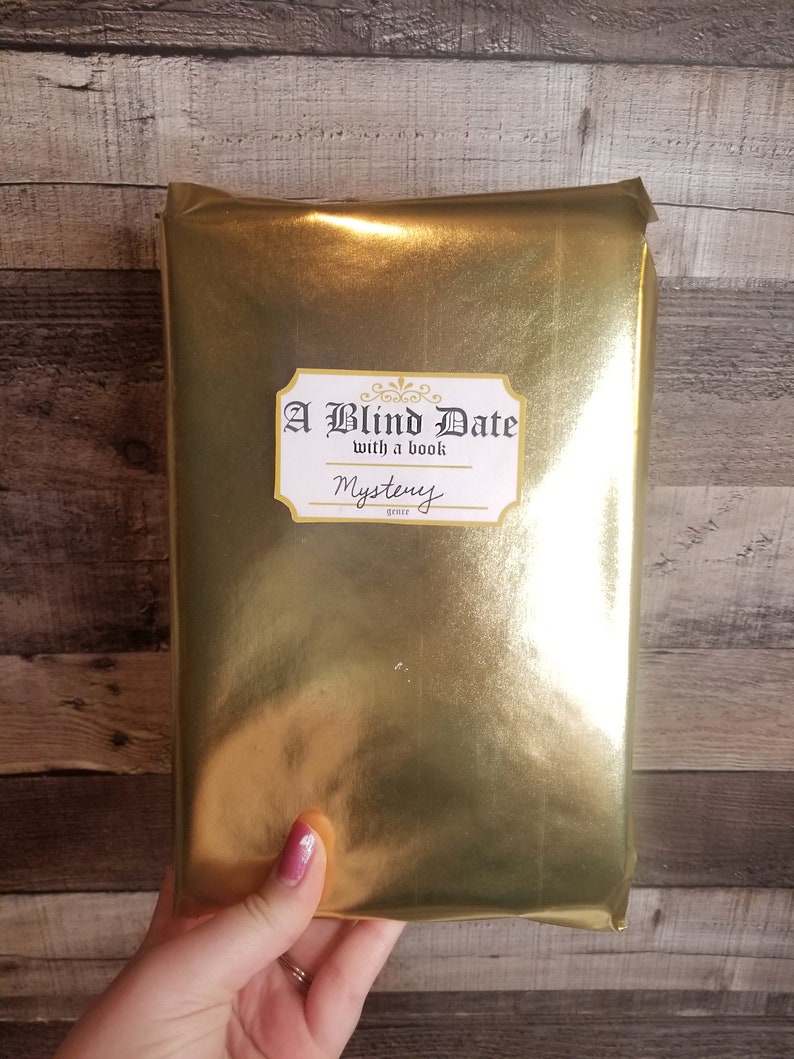 May include: A gold-wrapped book with a white label that reads "A Blind Date with a book" and "Mystery" genre.