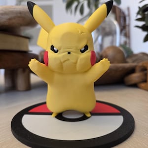 May include: A yellow Pikachu figurine with black-tipped ears, red cheeks, and an angry expression. The figure stands on a black, white, and red circular base, resembling a Poké Ball. The figurine is a collectible item.