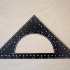 Puede incluir: Un transportador negro con una escala semicircular marcada en grados de 0 a 180. El transportador tiene un borde recto a cada lado.