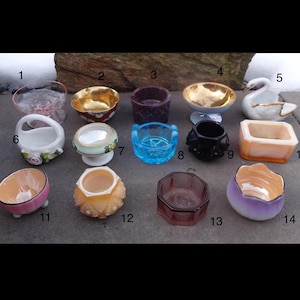 May include: A collection of fourteen small decorative bowls and dishes in various shapes, colors, and materials. Includes glass, ceramic, and porcelain pieces, some with gold accents, floral designs, and a swan-shaped dish. Ideal for display or small items.