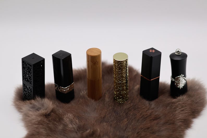 Puede incluir: Seis tubos de l&aacute;piz labial diferentes con varios dise&ntilde;os y colores. Los tubos est&aacute;n dispuestos en una fila sobre una superficie de piel marr&oacute;n. Los tubos est&aacute;n hechos de negro, oro y madera.