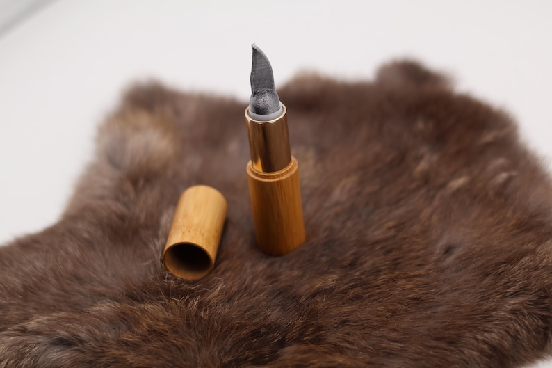 Puede incluir: Un tubo de madera con una punta gris puntiaguda y una banda de metal dorado. El tubo est&aacute; sobre una superficie de piel marr&oacute;n.