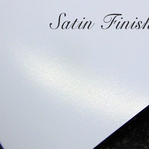 May include: A close-up of a white surface with a subtle, textured satin finish. The surface has a slight sheen and a smooth, even texture. The text "Satin Finish" is written in black cursive lettering at the top of the image.