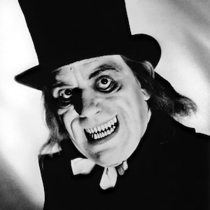 May include: A black and white photo of a man in a top hat and a dark suit, with a sinister smile. His eyes are wide and his teeth are sharp.