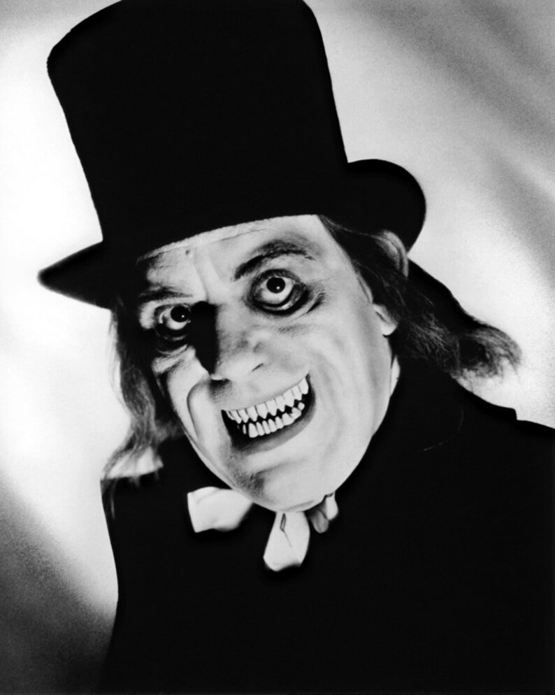 May include: A black and white photo of a man in a top hat and a dark suit, with a sinister smile. His eyes are wide and his teeth are sharp.