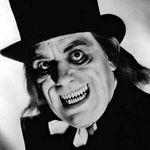 May include: A black and white photo of a man wearing a top hat and a sinister smile. He is dressed in a dark suit and has a long, dark beard. The photo is taken from a low angle, making the man appear even more menacing.