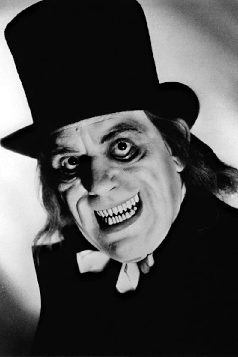 May include: A black and white photo of a man wearing a top hat and a sinister smile. He is dressed in a dark suit and has a long, dark beard. The photo is taken from a low angle, making the man appear even more menacing.