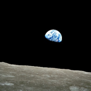 May include: A photograph taken from space showing the Earth as a blue and white sphere against a black background. The Earth is seen from a distance, with the moon's surface in the foreground.