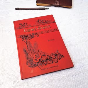 May include: A red hardcover book titled "LOEWE ALBUM" with gold lettering. The book has a black and white illustration of musical instruments and a tree on the front cover. The text "Band II" and "COLLECTION LITOLFF No 2343" are printed on the cover.