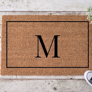 May include: A brown coir doormat with a black border and the letter "M" in the center.