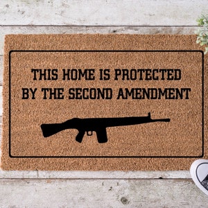 May include: A brown doormat with the text "This home is protected by the second amendment" and a silhouette of a rifle.
