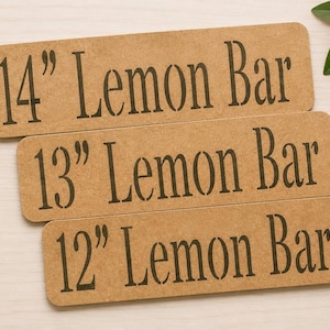 May include: Three rectangular tan signs with rounded corners, each featuring black stencil-style text. The top sign reads 14" Lemon Bar, the middle sign reads 13" Lemon Bar, and the bottom sign reads 12" Lemon Bar, all in a serif font.