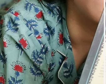 May include: A person wearing a blue and white floral print pajama top with a white trim. The person is holding a book with a decorative border.