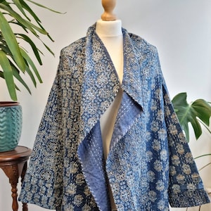 May include: A blue quilted jacket with a white floral pattern. The jacket has a shawl collar and is open in the front.