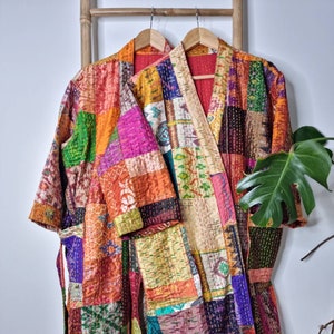 May include: Two colorful patchwork robes with a red lining hanging on wooden hangers. The robes are made of a variety of fabrics in shades of orange, pink, green, blue, and purple.