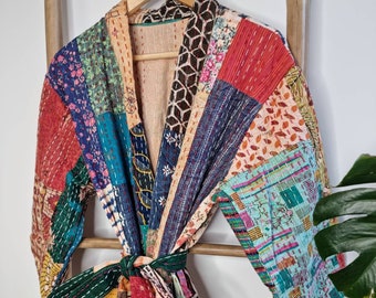May include: A colorful patchwork quilted robe with a tie belt. The robe is made of various fabrics in shades of blue, red, green, yellow, and brown. The robe is hanging on a wooden ladder.