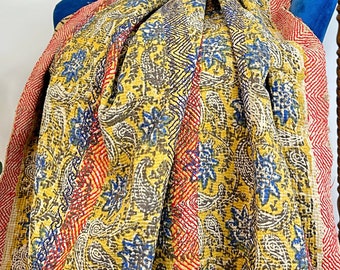 May include: A yellow, blue, and red kantha quilt with a paisley pattern draped over a blue armchair. The quilt is made of cotton and has a hand-stitched design.