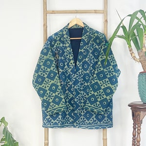 May include: A blue and green patterned jacket hanging on a wooden ladder. The jacket has a geometric design with a diamond pattern and floral motifs. The jacket is made of a soft, quilted fabric.