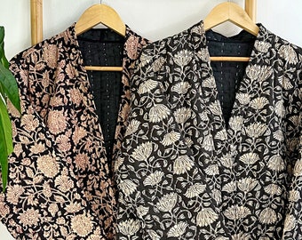 May include: Two black cotton jackets with floral patterns. One jacket has a pink floral pattern and the other has a white floral pattern. The jackets are hanging on a wooden rack.