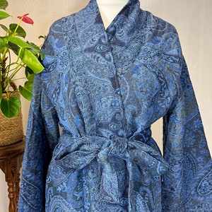 May include: A blue paisley patterned robe with a self-tie belt. The robe has long sleeves and a shawl collar.