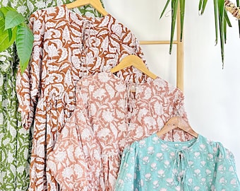 May include: Four floral print dresses hanging on a wooden rack. The dresses are in shades of green, brown, pink, and blue. Each dress has a white floral pattern.
