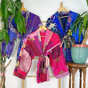 May include: Three quilted robes hanging on wooden hangers. The robe on the left is purple, the middle robe is pink and the robe on the right is blue.