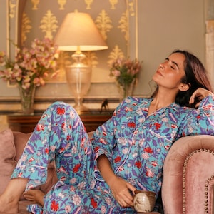 Peut inclure: Une femme portant un pyjama bleu et blanc &agrave; fleurs avec des accents rouges, se relaxant sur un canap&eacute; rose. Elle tient une tasse dans sa main.