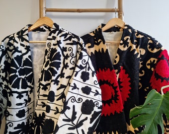 May include: Two embroidered jackets with floral patterns. One jacket is black with white and red embroidery, the other is white with black embroidery.