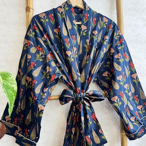 May include: A navy blue robe with a floral pattern of red and gold flowers and leaves. The robe has a white trim and a matching tie belt. It is hanging on a wooden ladder.