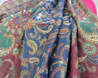 May include: A blue and burgundy paisley patterned throw blanket with a fringed edge. The blanket is draped over a pink chair.