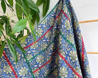 May include: A blue kantha quilt with a floral pattern and red and green stripes. The quilt is folded and draped over a wooden rack.