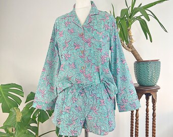 Op de afbeelding: Een tweedelige pyjamaset in lichtblauwgroen, met een bloemenpatroon in roze en groen. De top met lange mouwen heeft een kraag en een knoopsluiting. De shorts hebben een elastische tailleband. De set wordt op een mannequin getoond.