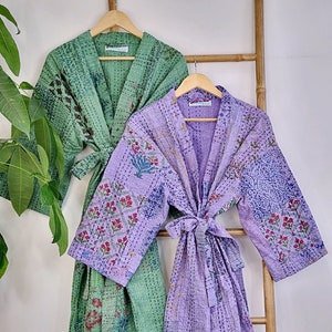May include: Two quilted robes hanging on a wooden ladder. The robe on the left is green with a floral pattern. The robe on the right is purple with a floral pattern.