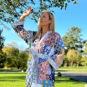 May include: A white quilted robe with a patchwork design featuring various floral and geometric patterns in shades of blue, pink, yellow, and red. The robe has a tie belt and a large pocket on the front.