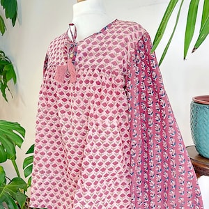May include: A pink and blue floral print cotton top with a tie at the neck and long sleeves. The sleeves are gathered at the cuffs.