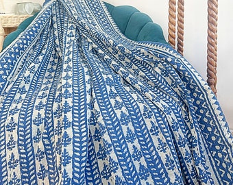 May include: A blue and white patterned cotton throw blanket draped over a teal sofa. The blanket features a repeating design of leaves and vines.