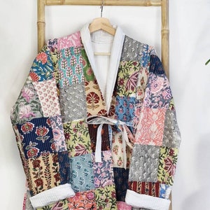 May include: A patchwork quilted jacket with a tie closure. The jacket is made of various fabrics with floral patterns in shades of pink, blue, green, and yellow.
