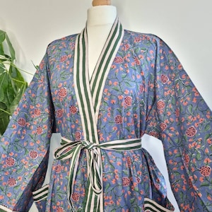 Könnte beinhalten: Eine blaue Baumwollrobe mit Blumendruck und grün-weiß gestreiftem Besatz. Die Robe hat einen Bindegürtel und zwei Taschen.