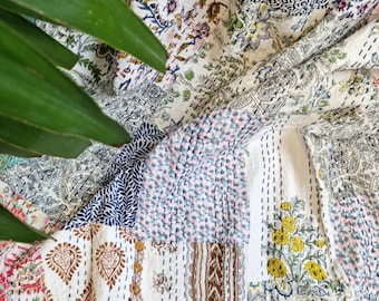 May include: A white cotton quilt with a patchwork design featuring various floral patterns in shades of pink, blue, yellow, and brown. The quilt is made of several different fabrics sewn together, creating a unique and textured look.