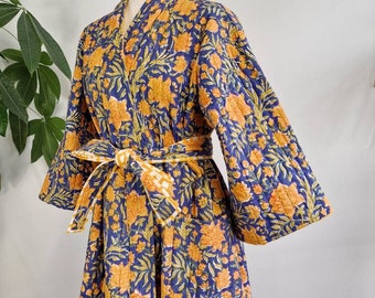 Puede incluir: Una bata acolchada con una base azul oscuro y un estampado floral naranja vibrante. La prenda tiene mangas largas y anchas, un escote en V y un cinturón de tela a juego en la cintura. La textura acolchada es visible en toda la pieza.