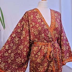 May include: A long, burgundy floral print robe with a matching sash. The robe has a V-neck and long sleeves with a contrasting orange and gold trim.