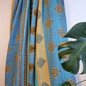 May include: A blue and gold kantha quilt with a paisley pattern. The quilt is hand-stitched and has a vintage look.