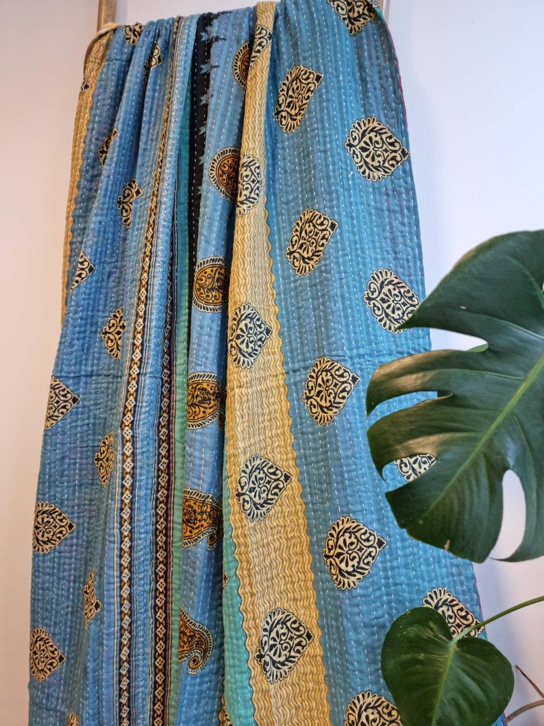 May include: A blue and gold kantha quilt with a paisley pattern. The quilt is hand-stitched and has a vintage look.