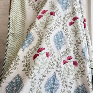 May include: White fabric with a floral pattern featuring pink flowers, blue decorative shapes, and green leaves. The fabric has a green and white chevron pattern on the reverse side.