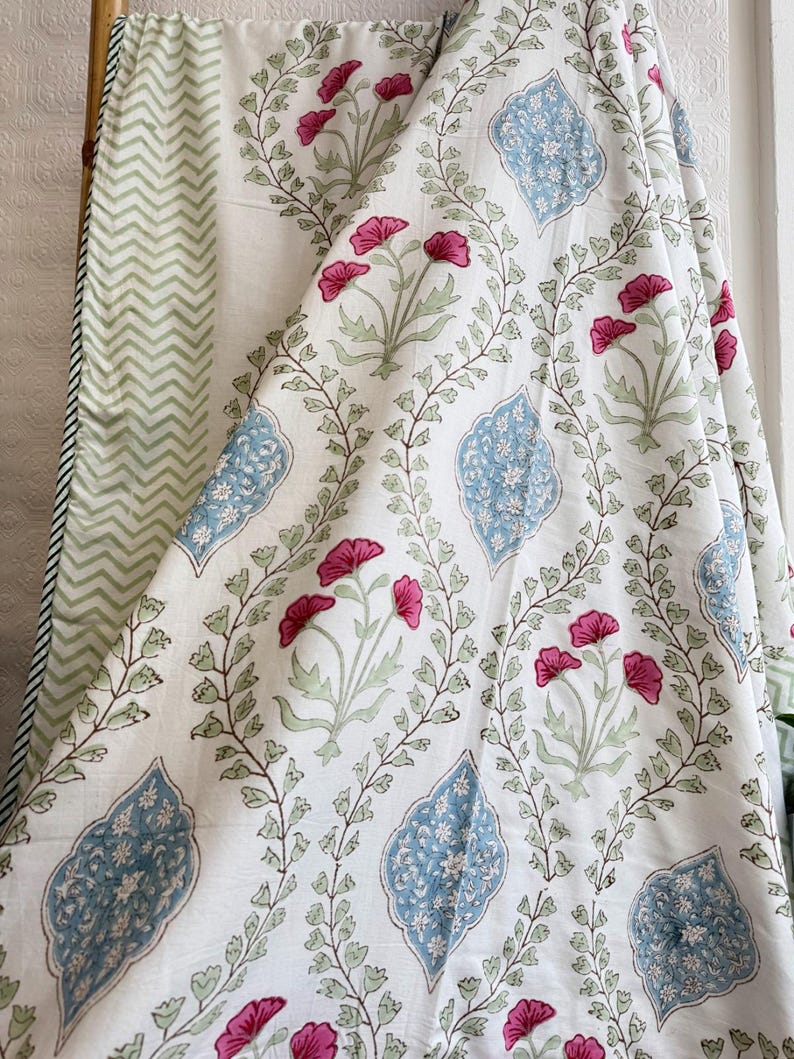 May include: White fabric with a floral pattern featuring pink flowers, blue decorative shapes, and green leaves. The fabric has a green and white chevron pattern on the reverse side.
