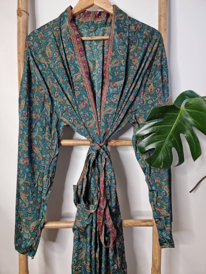 May include: A long-sleeved robe featuring a teal base color with an intricate multicolored paisley pattern in shades of pink, yellow, and orange. The garment includes a matching fabric tie belt at the waist and a contrasting border along the front opening.